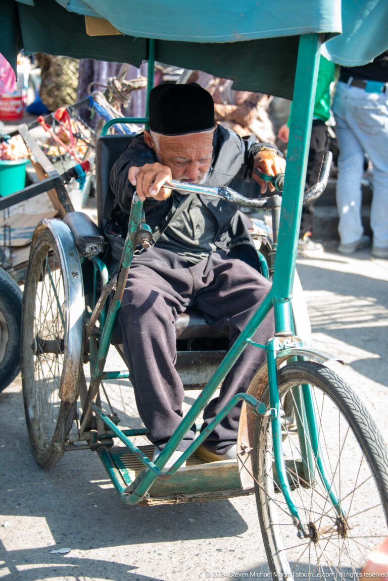 Close view of a seated rickshaw driver and bicycle frame.