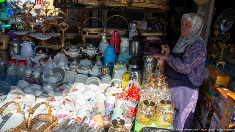 Woman vendor among glassware and decorative household items.