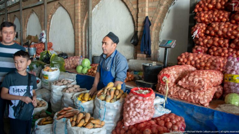 Woman seated among large sacks of onions and produce.