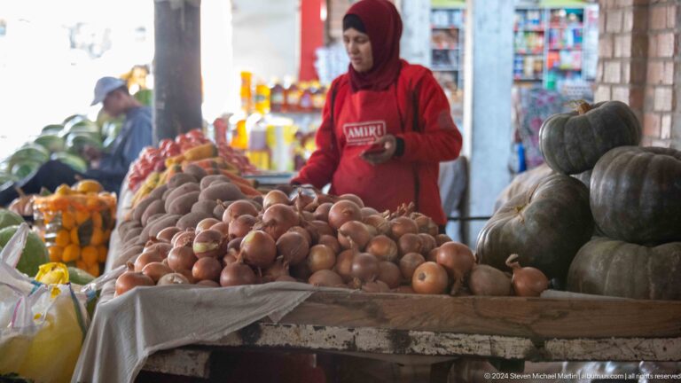 Vendor standing behind a large mound of potatoes.