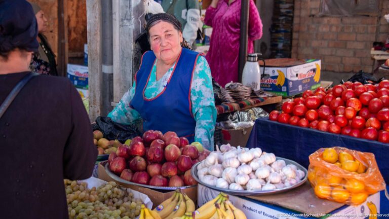 Woman vendor with apples, garlic, tomatoes, and peppers.