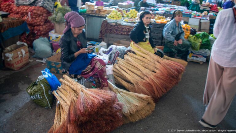 Vendors seated behind bundles of handmade brooms.