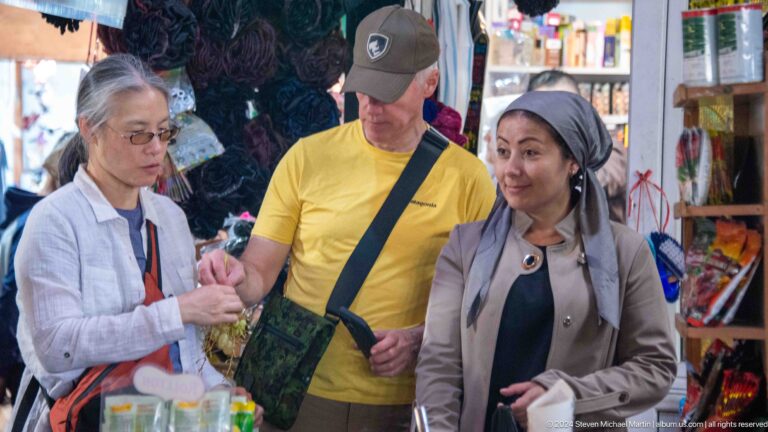Market conversation between visitors and a smiling woman.