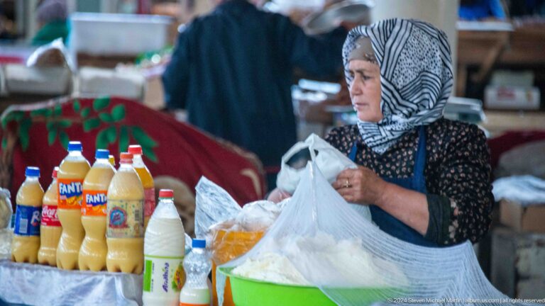 Woman bagging white dairy or grain product beside bottled drinks.
