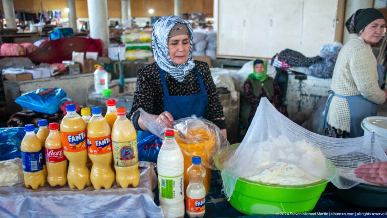 Woman vendor posing behind bottled beverages and a white food mound.