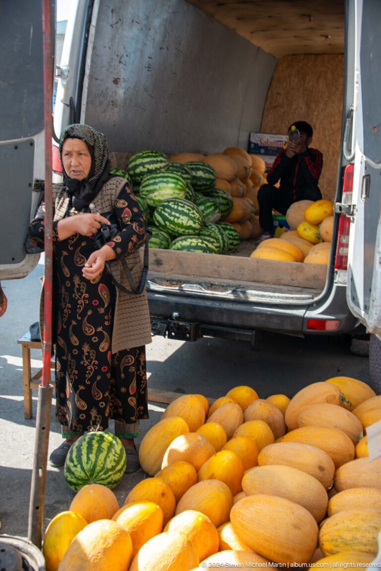 Woman beside a van loaded with watermelons and melons.