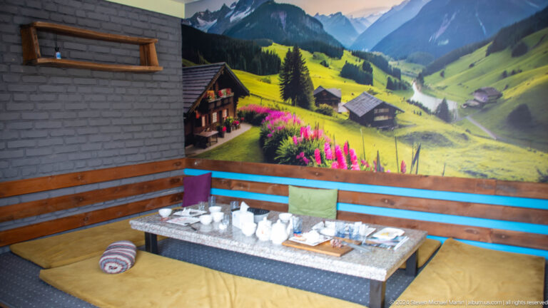 Indoor dining platform with low table and mountain mural.