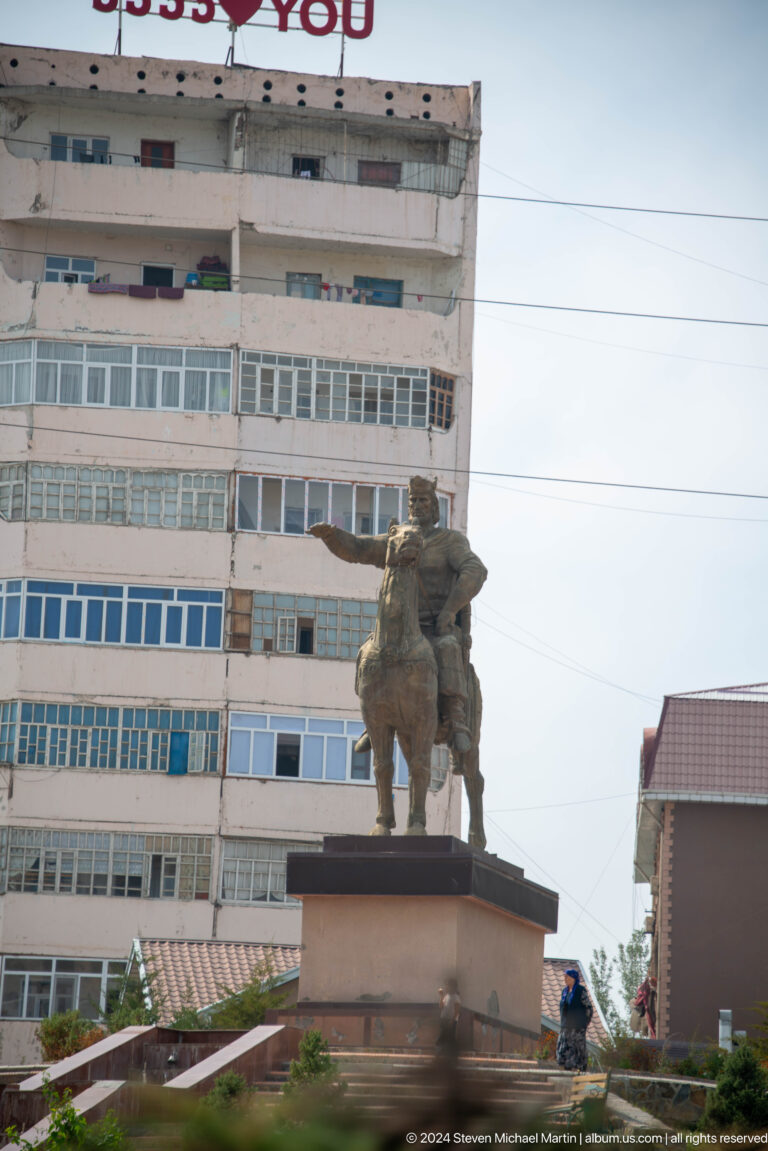 Public sculpture of a standing human figure before a building.