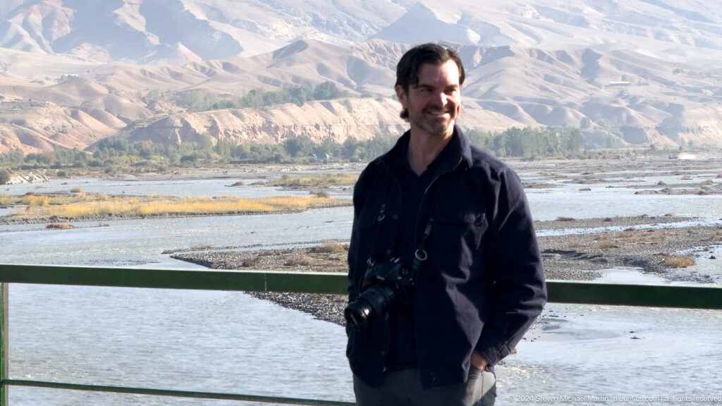 Male traveler standing beside the river with mountains behind.