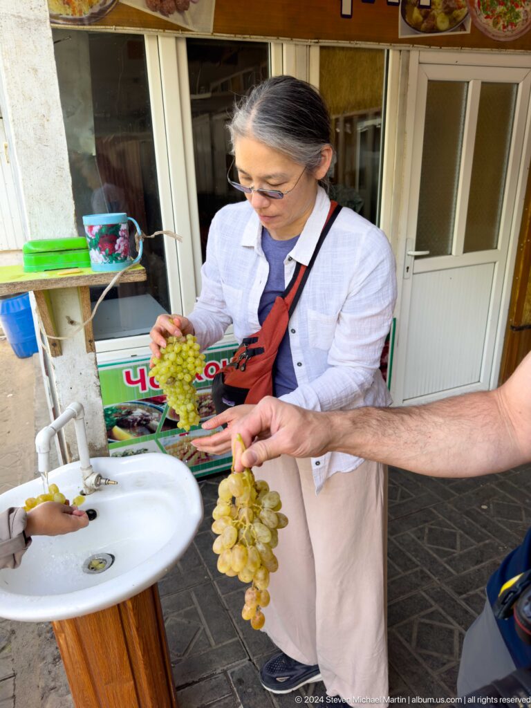 Woman offering fresh grapes outside a shop.
