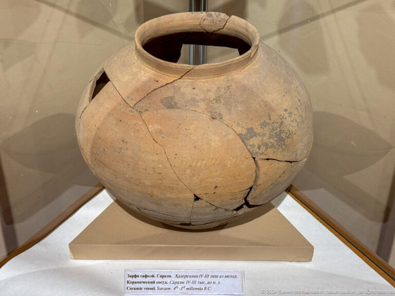 Large reconstructed buff ceramic jar with a wide mouth and visible cracks on a museum plinth.