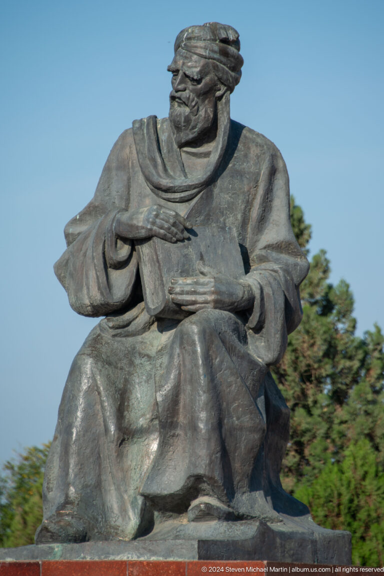 Close view of a seated bronze figure's robed torso and expressive hands.