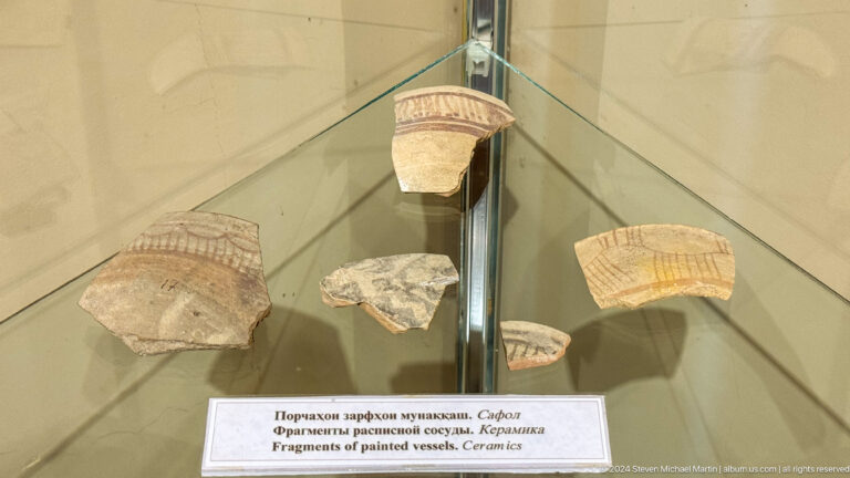 Five curved pottery fragments with banded decoration suspended inside a glass display case.