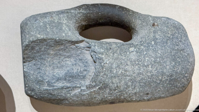 Close view of a heavy gray stone artifact with a large circular hole and worn worked surface.