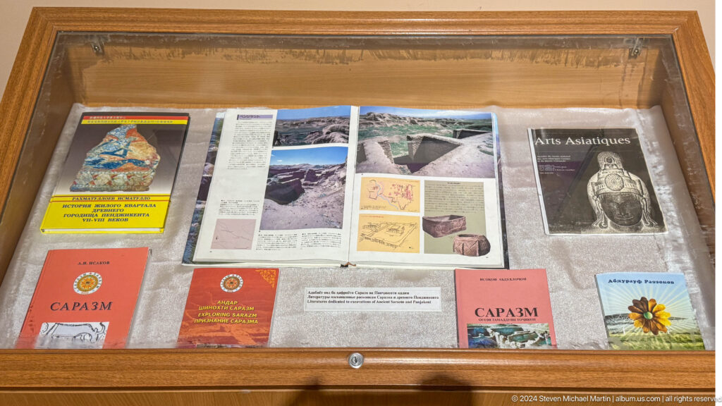 Open books, journals, site photographs, and archaeological plans arranged inside a wooden display case.