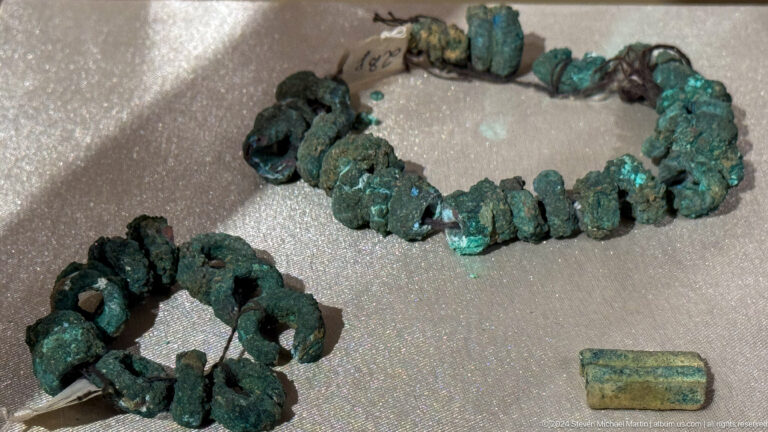 Close view of looped strands of irregular green-blue beads and corroded metal fittings.