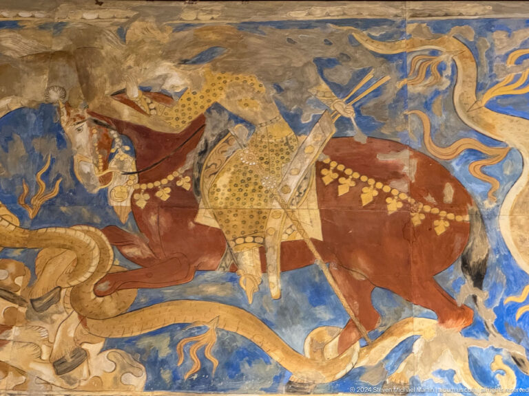 Armored rider on a red horse against a blue mural background.