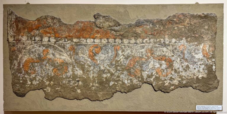 Long broken plaster fragment with a narrow faded band of red and gray paint.