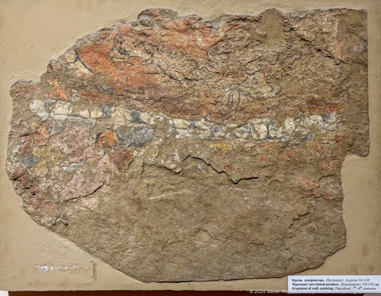 Broad irregular plaster fragment with faint reddish-brown painted traces.
