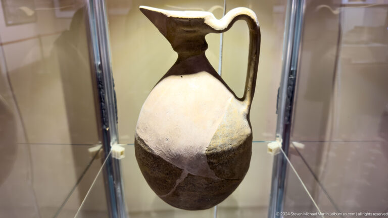 Tall two-tone ceramic pitcher with a black neck, loop handle, and pale angular body.