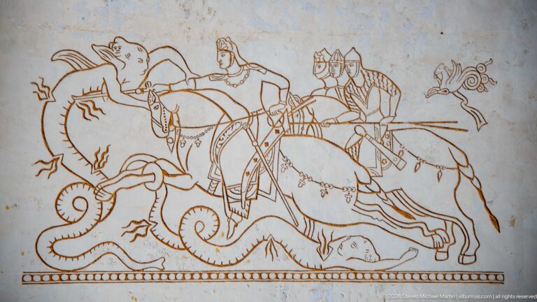 Brown line mural of historical riders on galloping horses across a pale exterior wall.