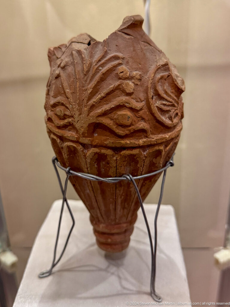 Close view of a reddish ceramic jar with raised swirling relief decoration.