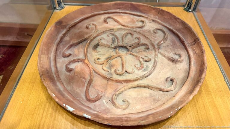 Round reddish ceramic dish with a central floral rosette and scrolling decoration.