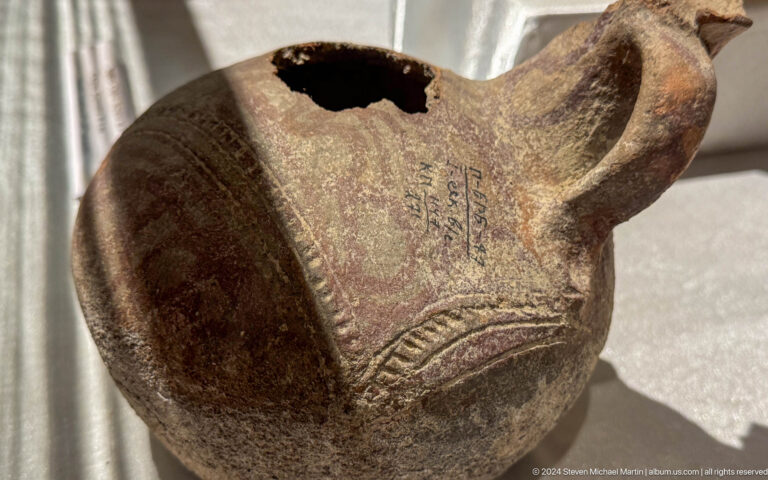 Dark brown ceramic ewer with a handle, open mouth, spout, and incised decoration.