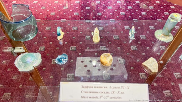 Small colorful beads, pendants, and fragments displayed on red patterned fabric.