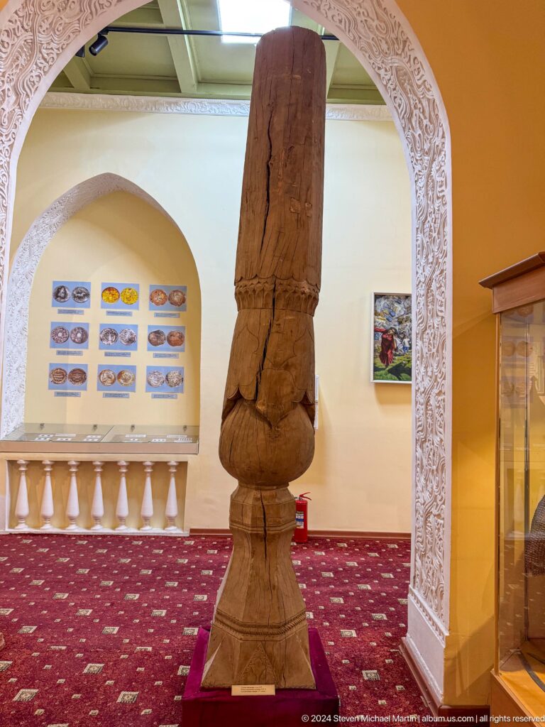 Close view of a dark carved wooden column with a bulbous transition and faceted shaft.