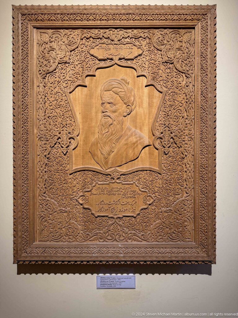 Carved wooden panel with a central profile portrait, inscription, and dense vegetal ornament.