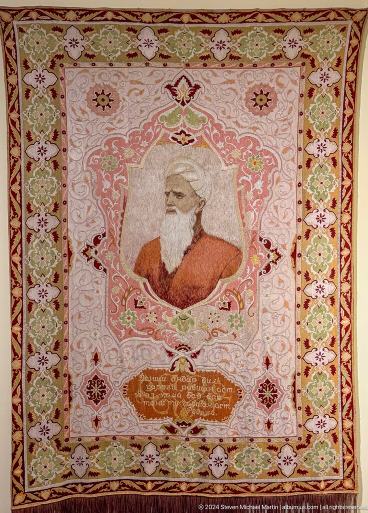 Portrait of an elderly bearded man in a white turban framed by floral ornament.