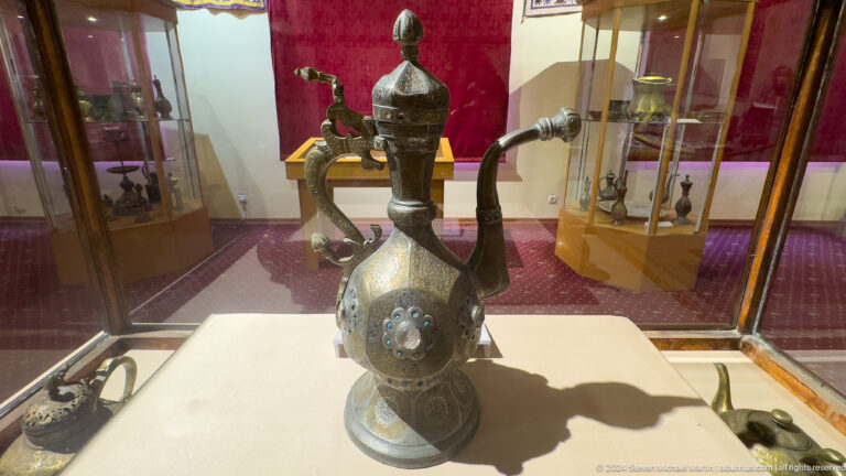 Dark metal ewer with a domed lid, curved spout, handle, and engraved body.