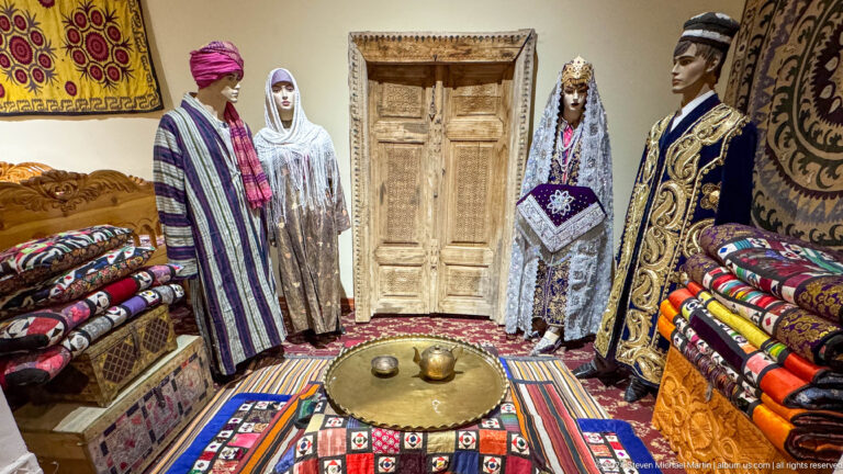 Traditional room reconstruction with mannequins in striped robes, a carved door, textiles, and a low table.