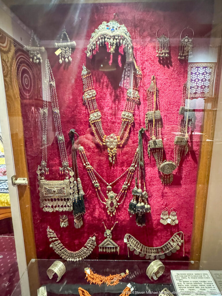 Silver-toned necklaces, pendants, chains, and amulets arranged on red velvet.