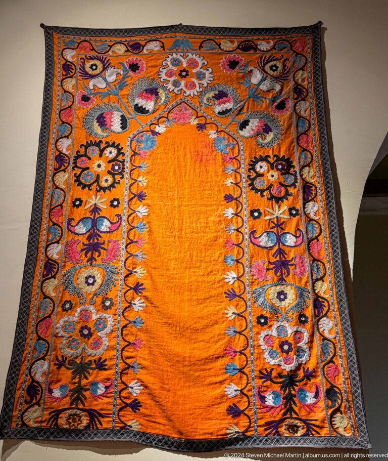 Orange textile panel with dense black, blue, and floral embroidered borders.