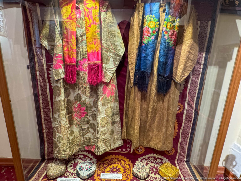 Long red, gold, green, and blue embroidered robes hanging together in a display.