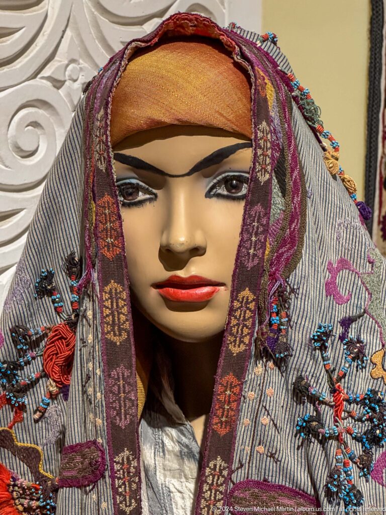 Female mannequin wearing a patterned veil with tassels and metal side ornaments.