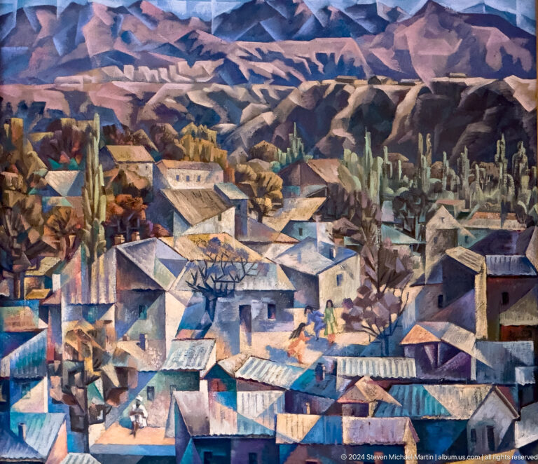 Colorful painting of a dense mountain town with blue-gray roofs and peaks behind.