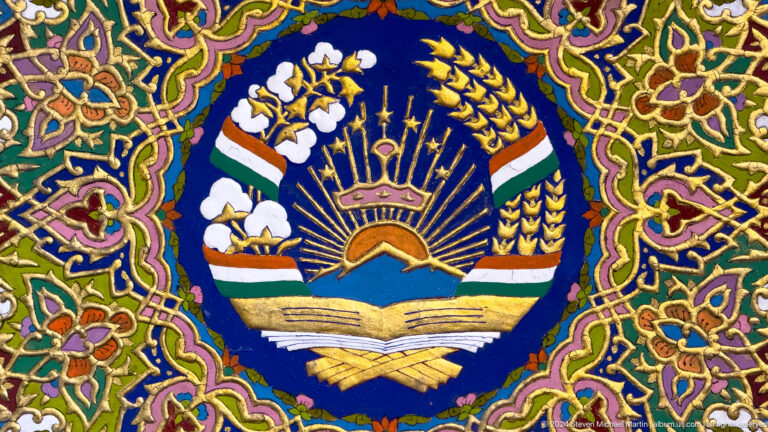 Embroidered Tajik national emblem with crown, seven stars, mountains, sun, wheat, and cotton.