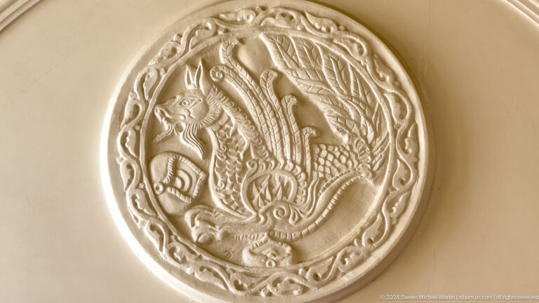 Round silver-toned medallion embossed with a bird and scrolling vegetal ornament.