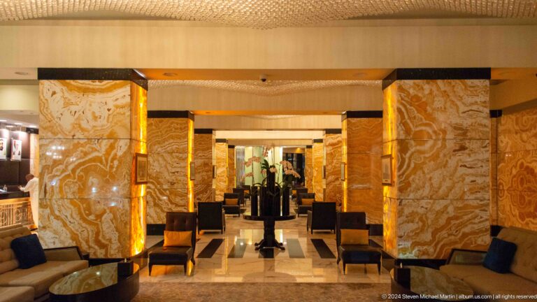 Symmetrical view down an Abu Dhabi luxury hotel lobby with polished stone wall panels, warm gold-toned lighting, and formal armchair seating arranged along a strong central axis through multiple rooms.