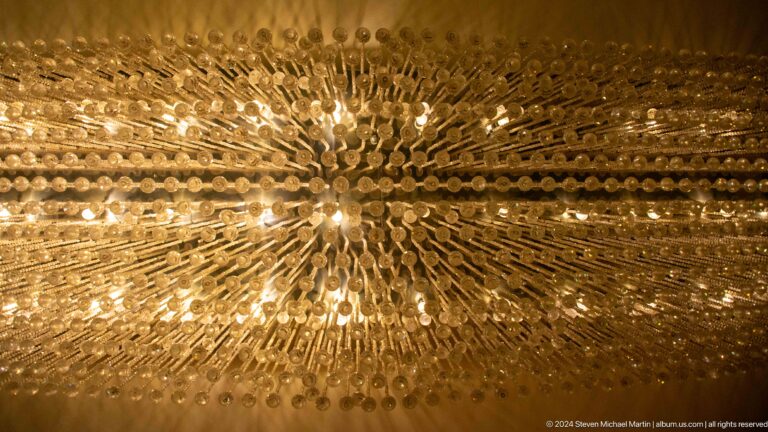 Upward close view of a starburst chandelier with hundreds of reflective elements radiating from a bright center in warm golden light.