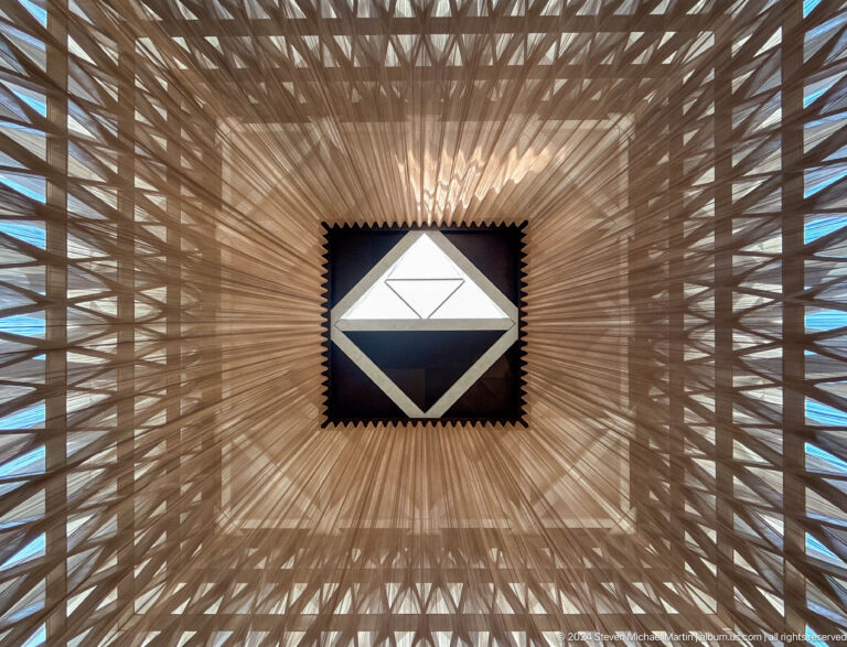 Upward view of the Abrahamic Family House worship interior ceiling, showing a pyramidal lattice converging on a bright square skylight at the center.