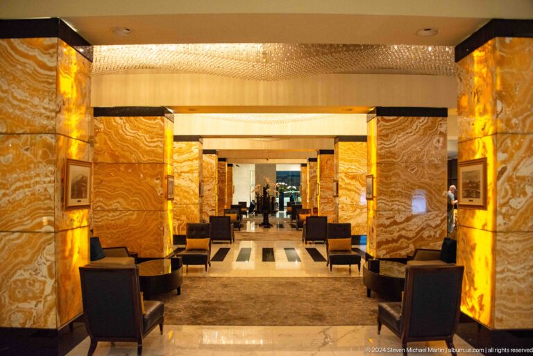 Symmetrical view down an Abu Dhabi hotel lounge, with two glowing backlit stone columns framing a central opening and dark upholstered seating arranged on both sides.