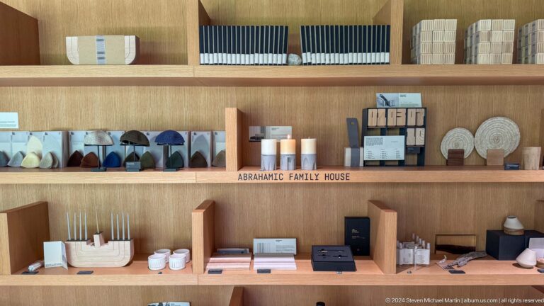 Wooden shelves in the Abrahamic Family House gift shop displaying neatly arranged ceramic vessels, books, and ABRAHAMIC FAMILY HOUSE branded merchandise.