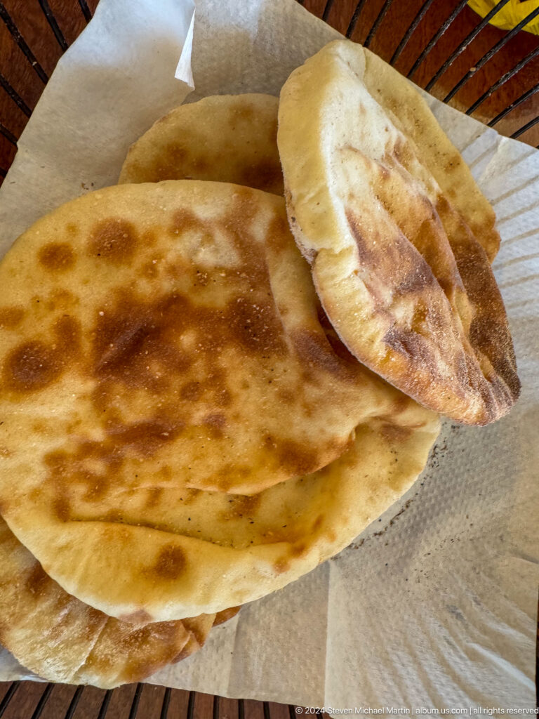 Close-up of Middle Eastern flatbreads in Abu Dhabi, including a large round flatbread and a smaller filled bread, showing browned, blistered surfaces and toasted spots.