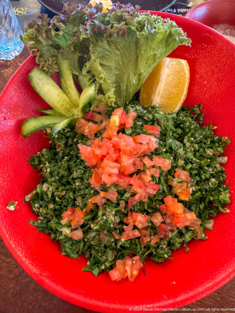 Overhead close-up of a plate of tabbouleh salad made of finely chopped parsley with diced tomato and a lemon wedge on the side.