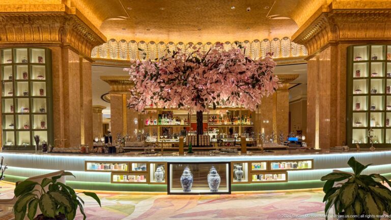 Frontal view of the Emirates Palace Mandarin Oriental lobby reception counter, dominated by a dense pink floral installation framed by gold columns and an ornate ceiling.