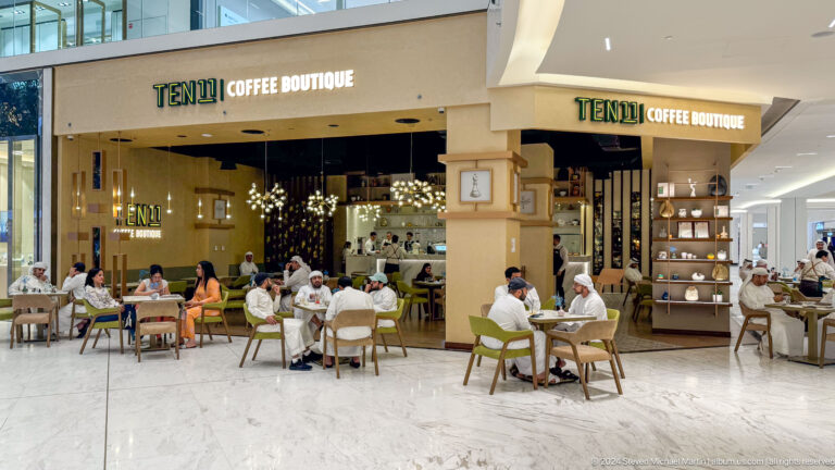 Open-plan Tuk Tuk Coffee House in an Abu Dhabi shopping mall with customers seated at white tables spilling into the mall corridor.